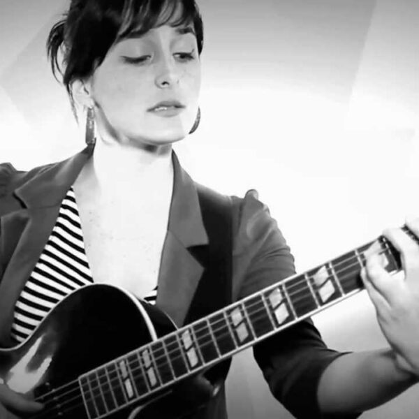 A black and white photo of Camila Meza holding a guitar